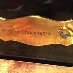 Auf dem Bild ist ein Klingelschild zu sehen, auf dem steht "Ring for Champagne"