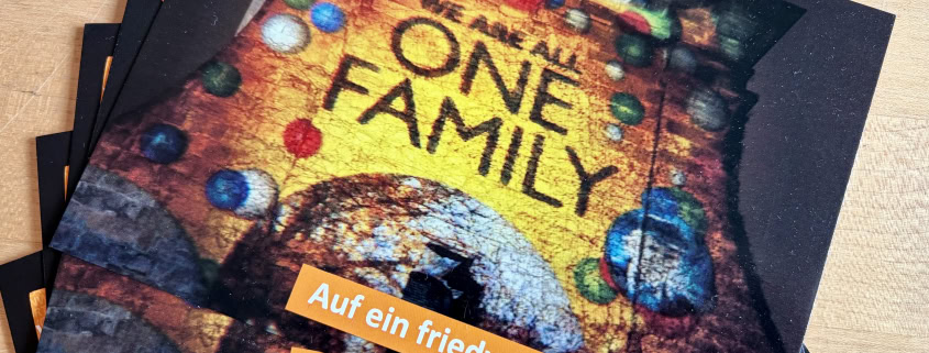 Foto: aufgefächerte Weihnachtskarten aus dem Wortladen. Ein friedvolles neues Jahr wird gewünscht, als Motiv ist eine beleuchtete Kirche zu sehen, auf der „We are all one Family“ projiziert wurde.